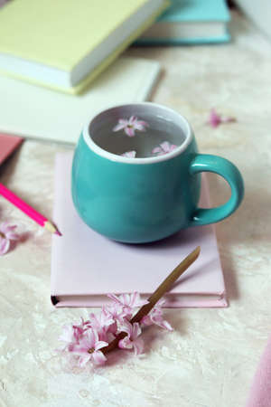 Cup with water and fresh hyacinth flowers, books, notepads, woolen pink sweater on a light background, at home, romantic congratulation, emotion of loveの写真素材