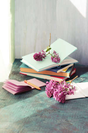 Books, notepads and fresh lilac flowers on table by the window, home schooling concept, back to...