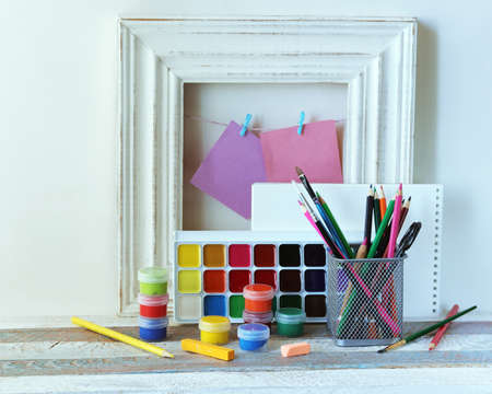 Paints, colored pencils and blank notebook on the background of the frame on a wooden table, the concept of learning, drawing lesson, back to schoolの写真素材