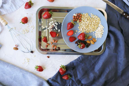 Healthy breakfast ingredients on the table, strawberries, oatmeal and nuts on a light background