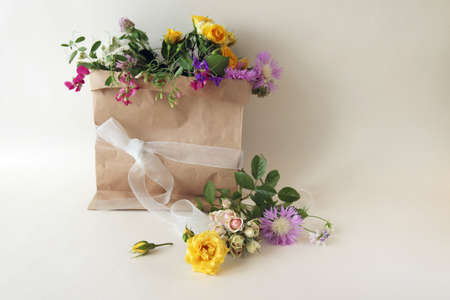 Bouquet of fresh roses, a package with wildflowers on a light background with a place for an...
