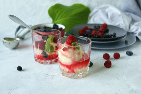 Homemade ice cream poured with fruit syrup and sprinkled with fresh berries, on a white table, healthy food, seasonal productsの写真素材