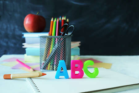 Pencils, multicolored letters, stack of books and apple on school board background, learning...