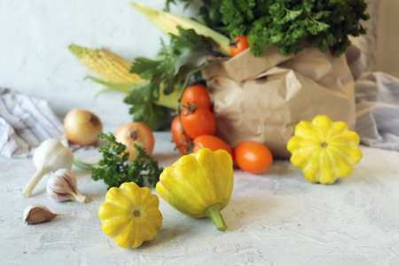 Fresh ripe variety of vegetables and greens in an ecological paper bag, on a light background,...