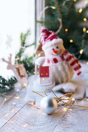 Christmas toys, a snowman and a house, balls, spruce branches, illumination on a wooden windowsill, winter, holidayの写真素材