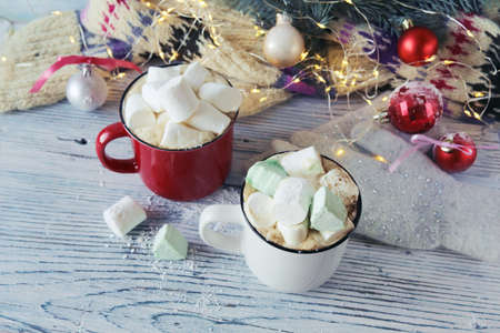 Cups of coffee with marshmallows, fir branches, Christmas decorations and illumination on a wooden...