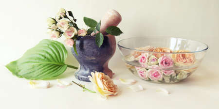Pink fresh rose, bowl of water with roses and flower petals, mortar on light background, body care,...