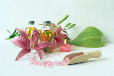 Pink lilies, burning candles, sea salt, oil and tincture of medicinal plants on the table, spa, useful and aromatic cosmetics for care and relaxationの写真素材