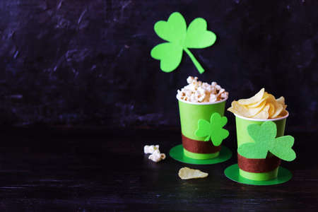 Popcorn and chips in green paper glasses in the shape of St. Patrick's hat, background decorated...
