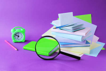 Books, magnifying glass, alarm clock and notepads, pastel colored paper, on the table, purple background, the concept of learning, education, back to school, holidays, readingの写真素材