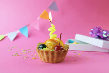 Birthday cupcake decorated with fruit jelly and a burning candle, holiday decorations, gifts on a...