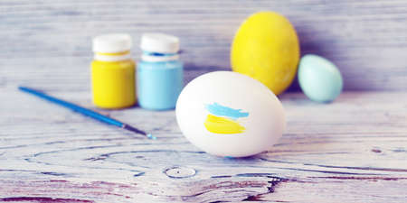 White chicken eggs, yellow and blue paints and brushes on the table concept, symbol, Ukraine,...