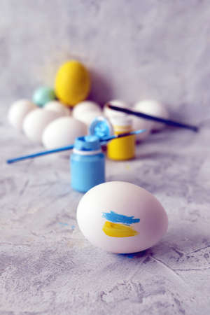 White chicken eggs, yellow and blue paints and brushes on the table concept, symbol, Ukraine,...