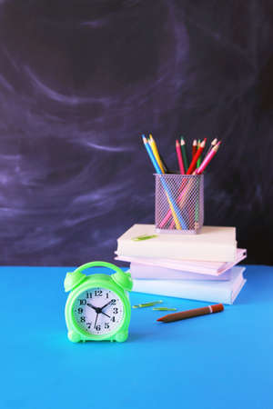 Alarm clock on the background of a stack of books, pencils and a chalkboard, on the table, back to school, education, studyの写真素材