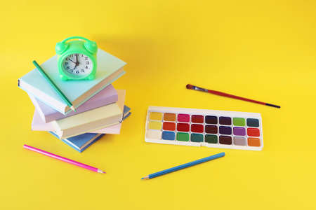 Alarm clock, stack of books and stationery on yellow background, back to school, holidays, education and learningの写真素材