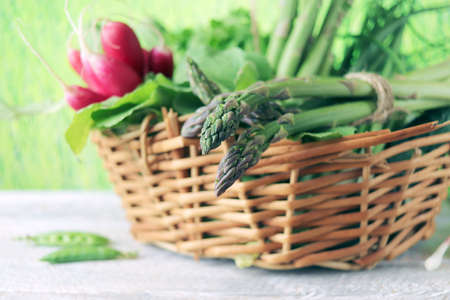 Asparagus, radishes and green onions in a wicker basket, on a wooden table, against the backdrop of a lawn, harvest season, organic natural food, healthy food, home cookingの写真素材