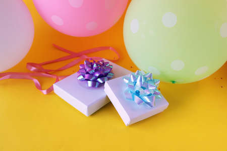 Gift boxes decorated with a bow of shiny ribbon, holiday balloons, bright yellow background, concept...