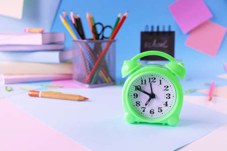 Alarm clock, books and stationery on pastel colors background of colorful paper, back to school,...