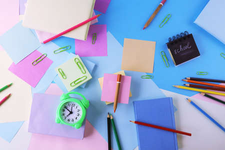 Stationery, alarm clock, books on a background of pastel colors of multi-colored paper, back to school, education, schoolchild study table, copy space, top viewの写真素材