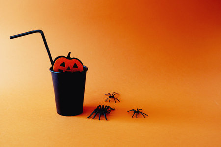 Halloween holiday concept. Black paper cup with drinking straw and spiders on orange background.の写真素材