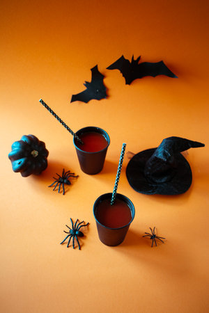 Halloween party concept. Glass of juice with straw, paper bats and spiders on orange background.の写真素材