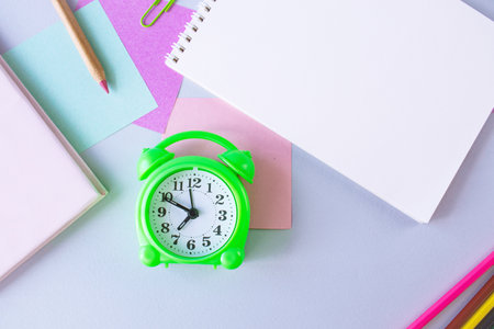 Green alarm clock with blank notebook and pencil on colorful paper background.の写真素材