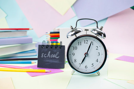 Alarm clock and school supplies on colorful paper background. Back to school concept.