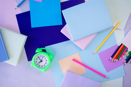 Colorful paper sheets, pencils and alarm clock on colorful background