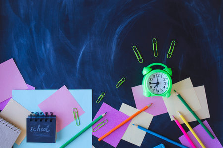 Back to school concept with alarm clock and stationery on blackboard backgroundの写真素材