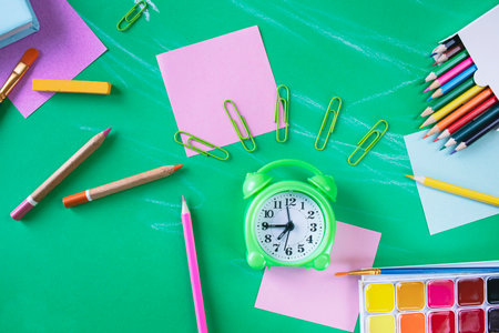 School supplies and alarm clock on green background. Back to school concept.の写真素材