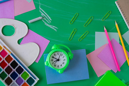 Back to school concept with alarm clock and stationery on green background