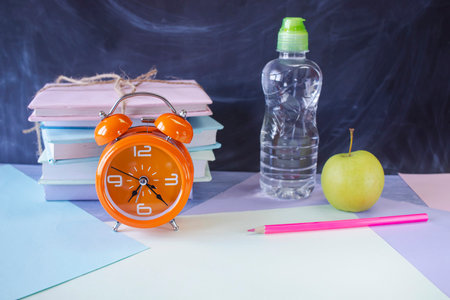 Back to school concept with alarm clock, books and water bottle.