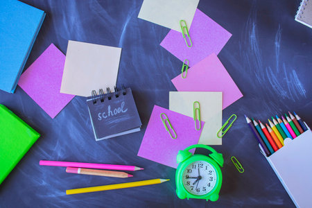 Back to school concept. School supplies and alarm clock on blackboard background