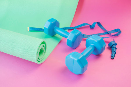 Dumbbells, yoga mat and measuring tape on pink background