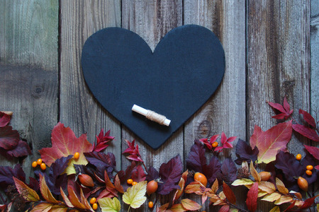 Background with autumn leaves, slate heart and chalk on wooden boards