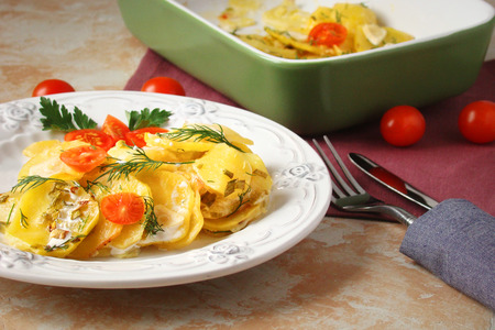 potato gratin with cheese, cream, tomatoes and greens on a white plateの写真素材