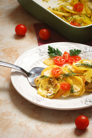 potato gratin with cheese, cream, tomatoes and greens on a white plateの写真素材