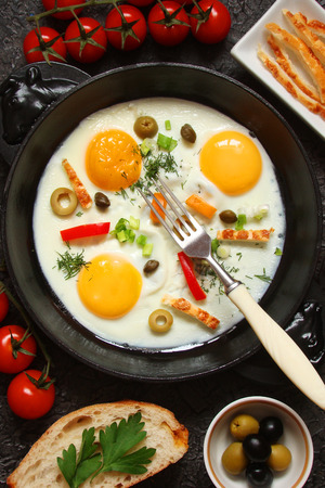 Fried eggs in a cast iron pan with peppers, tomatoes, capers, herbs and bread and olivesの写真素材