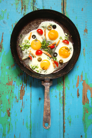 Fried eggs in a cast iron pan with peppers, tomatoes, capers, herbs and bread and olivesの写真素材