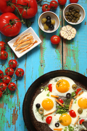 Fried eggs in a cast iron pan with peppers, tomatoes, capers, herbs and bread and olivesの写真素材