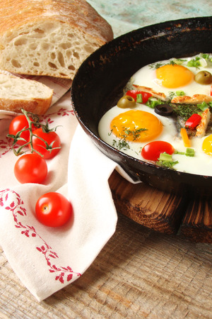 Fried eggs in a cast iron pan with peppers, tomatoes, capers, herbs and breadの写真素材