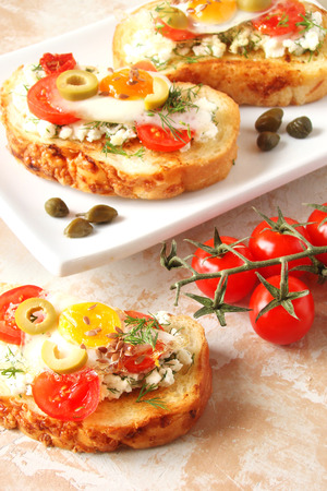 Bruschetta, crostini with cream cheese, with cherry tomatoes, herbs, olives, capers and fried egg の写真素材