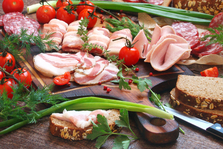 Delicatessen, smoked meat, bacon, vegetables, tomatoes, parsley on a wooden boardsの写真素材