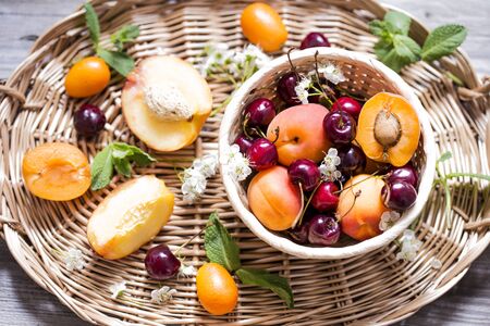 Fresh fruit apricots and cherries in wicker basket with mint leavesの写真素材