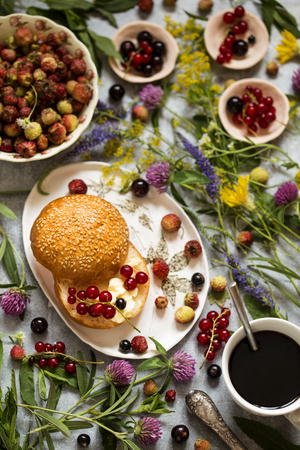 Summer Breakfast muffin, cream cheese, fresh berries currants, strawberries on a wooden background with wild flowersの写真素材