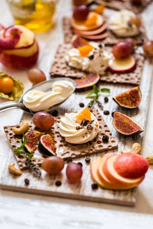 Crackers, crispbread crackers, figs and ricotta cheese are ready for the healthy food, grapes, Cape gooseberries, mint, Apple and chocolate on a light backgroundの写真素材