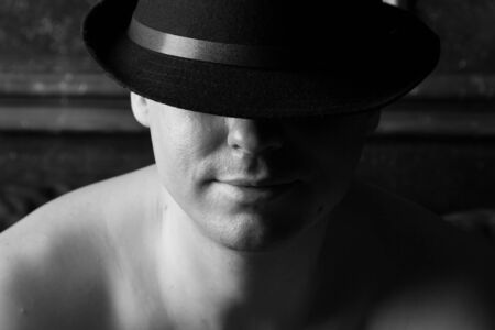 Man in a black hat with naked shoulders. Black and white. Selective focus.の写真素材