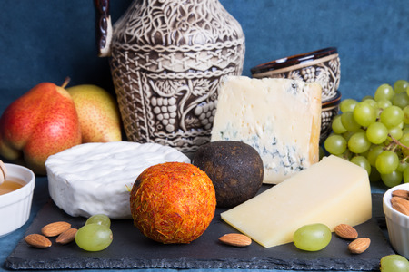Cheese plate. 5 species of cheese, fruit, nuts, wine jug. Close-up, selective focus.の写真素材