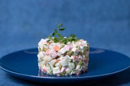 Olivier salad on a blue plate, decorated with pea sprouts. Traditional New Year and Christmas Russian salad. Close-up, selective focus, blue background.の写真素材
