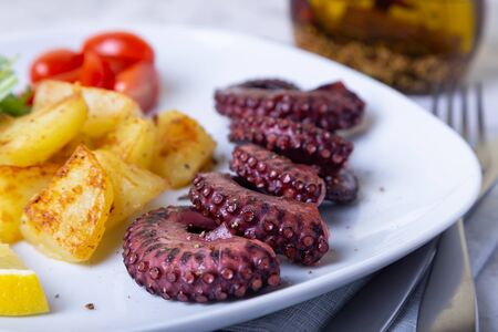 Grilled octopus with fried potatoes, arugula, tomatoes and lemon. Close-up.の写真素材